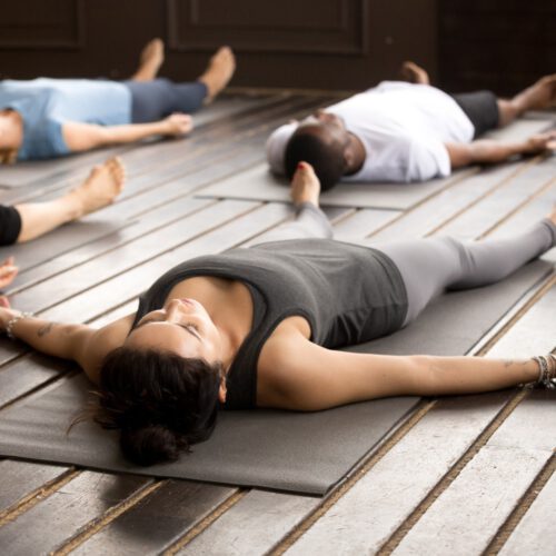 Group of young afro american and caucasian sporty people practicing yoga lesson lying in Dead Body pose, Savasana exercise, working out, resting after practice, indoor close up, studio